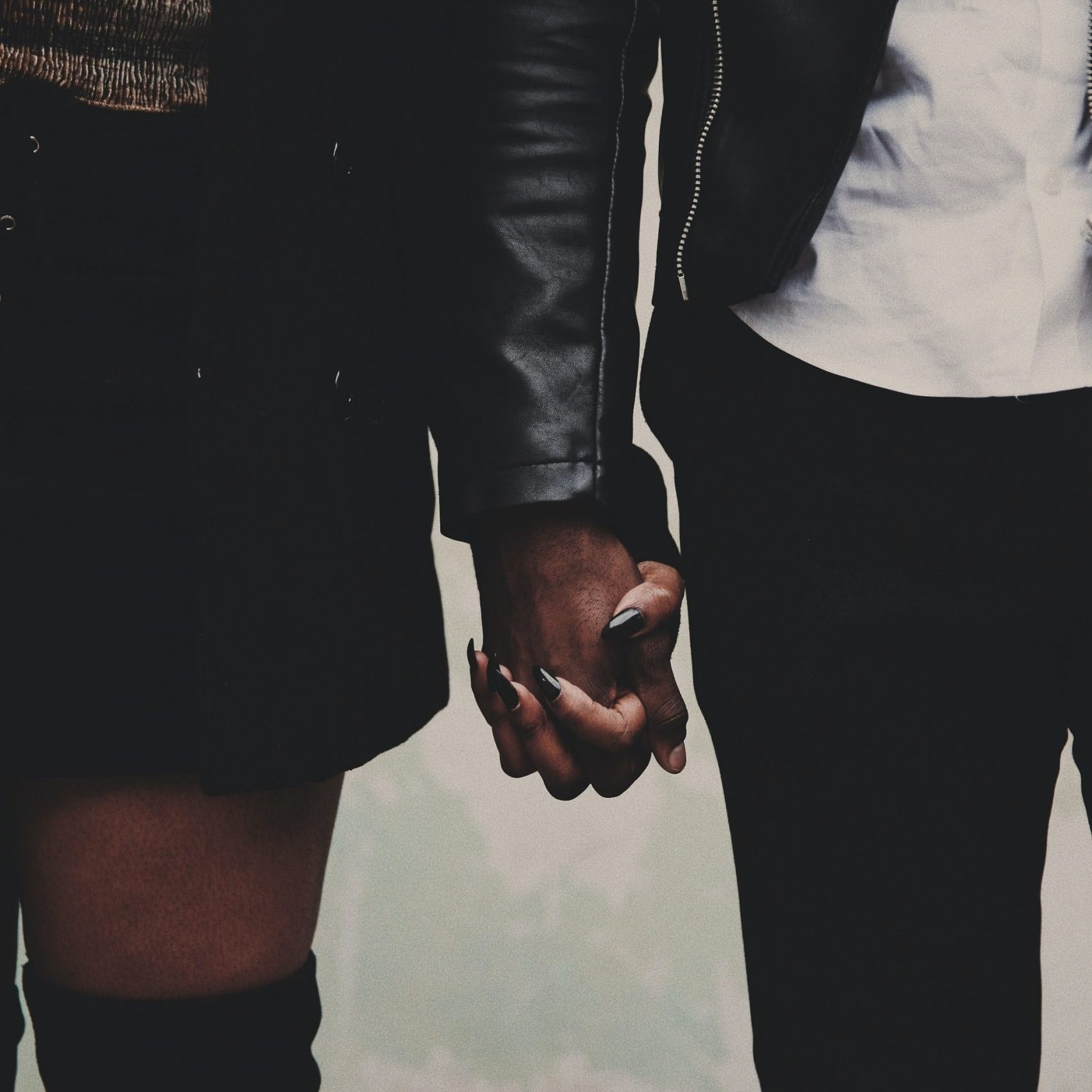A close up photo of the torsos of two people are holding hands